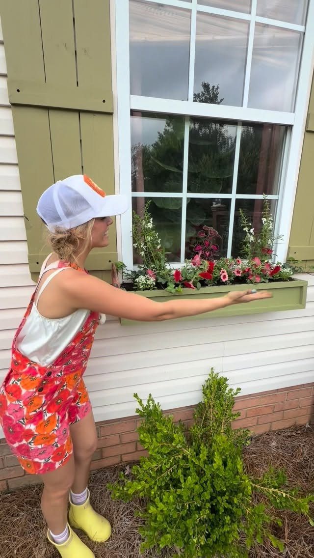 16 Small Home Landscaping Ideas That Fit Any Plot 2 A woman holding a green window box filled with red and white flowers against a house.